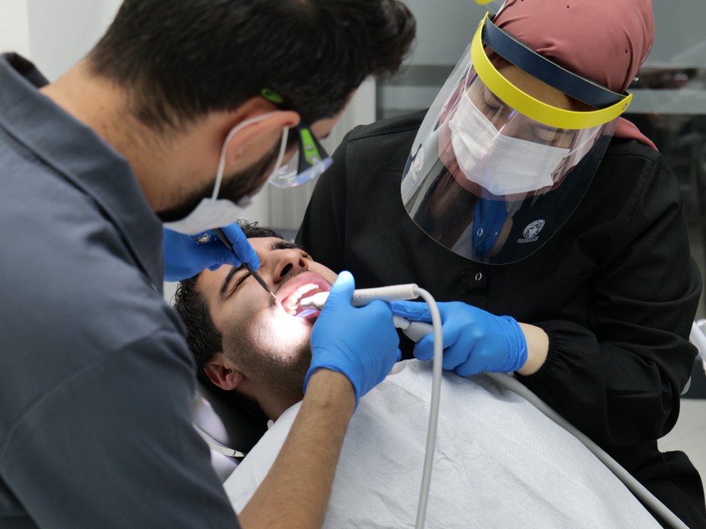 Dentist and assistant performing a dental procedure with suction and instruments.